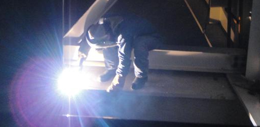 An ironworker welding a bridge at night representative of work that requires AISC certification.